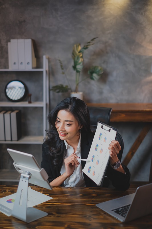 Asian Business woman is using tablet for video call connection or presenting project result by graph. Female entrepreneur, owner manager having positive energy while present goal of company planning